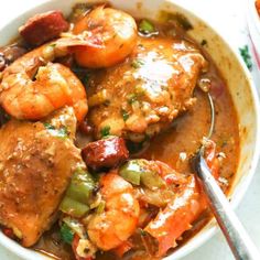 a bowl filled with shrimp and vegetables on top of a white tablecloth next to a spoon