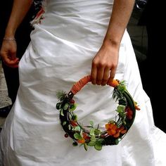 a woman in a white wedding dress holding a green and orange flowered wreath on her back