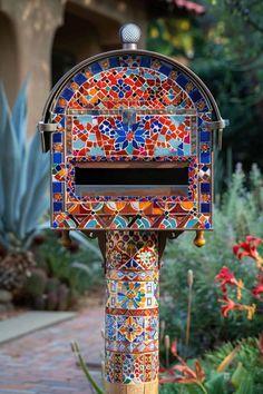 a colorful mailbox sitting on top of a brick walkway next to flowers and plants