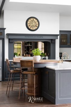 a kitchen with an island and stools next to a clock on the wall above it