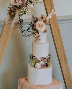 a three tiered wedding cake with flowers and feathers on the top is displayed in front of a ladder