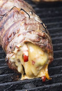 a piece of meat is being cooked on a bbq grill with cheese and sauce