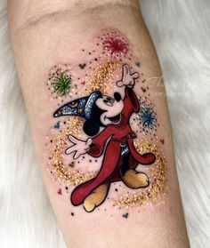 a mickey mouse tattoo on the left leg with gold glitters and stars around it