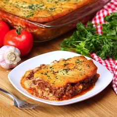 a white plate topped with lasagna covered in sauce next to tomatoes and parsley