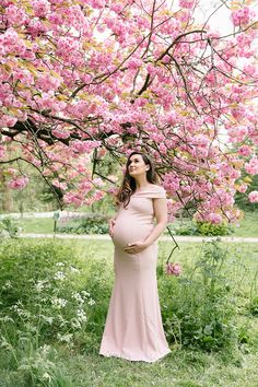 a pregnant woman standing in front of a tree with pink flowers