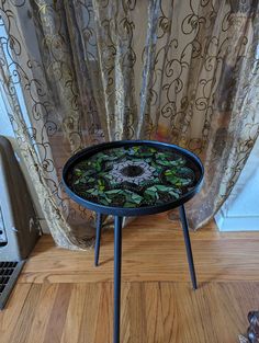 a black table with green plants on it sitting in front of a curtained window