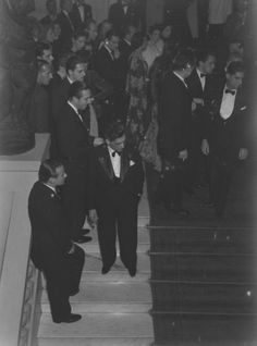 black and white photograph of men in tuxedos walking down the stairs at an event