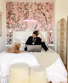 a woman sitting on a bed with a laptop computer and dog in front of her