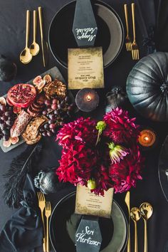 a table set with black plates, silverware and red flowers