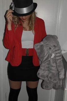 a woman in a red jacket and black skirt holding an elephant stuffed animal next to her