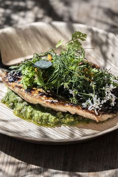 a white plate topped with fish covered in green sauce and garnished with herbs