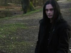 a man with long hair standing in the woods