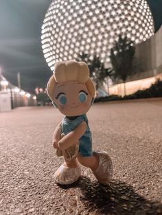 a little boy doll sitting on the ground in front of a large ball at night