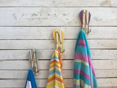 three towels hanging on the side of a wooden wall next to hooks and towel holders