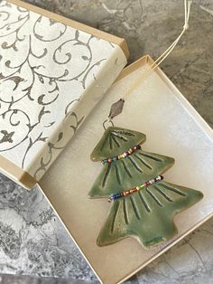 a green ceramic christmas tree ornament in a gift box on a marble table