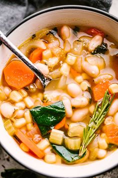 a white bowl filled with beans, carrots and spinach on top of a table