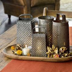 three metal canisters sitting on top of a wooden table next to a candle