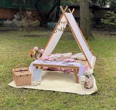 a bed with pillows and blankets on it in the grass near a picnic table that has a canvas tent over it