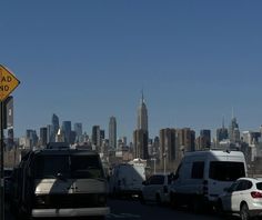 there are many cars and trucks on the road in front of the cityscape