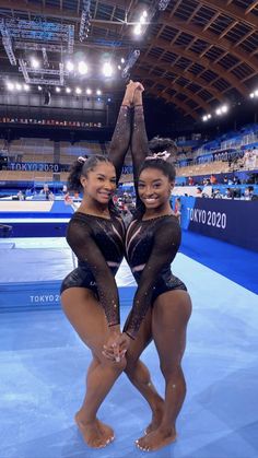 two women in black leotards standing next to each other on a blue floor