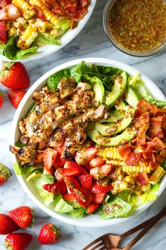 two bowls filled with salad and strawberries on top of a marble table next to silverware