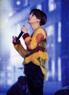 a woman standing on top of a stage with a microphone in her hand and wearing a colorful sweater