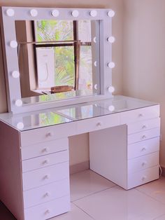 a white vanity with lights on it in front of a window and a large mirror