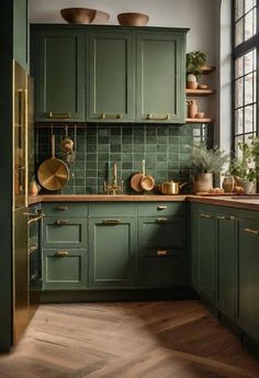 a kitchen with green cabinets and wooden floors, gold pulls on the cupboards as well as pots and pans