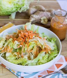 a white bowl filled with lettuce and carrots on top of a wooden cutting board