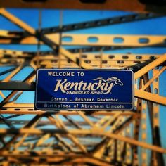 there is a sign on the bridge that says kentucky and it is blue with white lettering