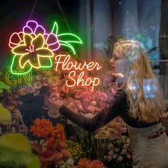 a woman standing in front of a flower shop sign with flowers on display behind her