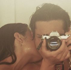 a man and woman kissing while holding up a camera