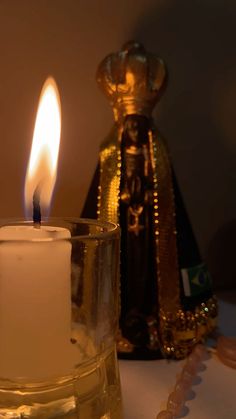 a lit candle sitting on top of a table next to a glass vase with a gold decoration