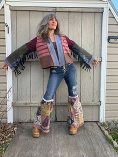 a woman standing in front of a shed wearing boots and a jacket with fringes