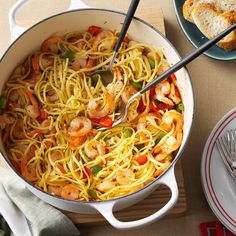 a pan filled with pasta and shrimp on top of a wooden table next to bread