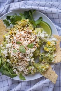 a white plate topped with guacamole and tortilla chips next to lime wedges