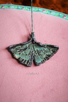 a small green butterfly sitting on top of a pink pillow next to a piece of string