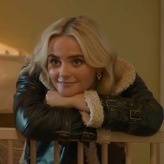 a woman with blonde hair wearing a black leather jacket leaning on a white railing looking at the camera