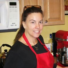 a woman in an apron is holding a red blender and smiling at the camera