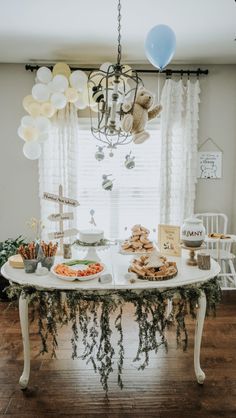 a white table topped with lots of food next to a window covered in balloons and streamers