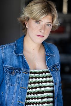 a woman with short hair wearing a jean jacket and striped shirt is looking at the camera