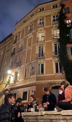 people are sitting on the steps in front of an old building at night with lights on