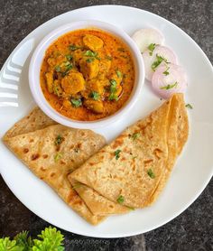 a white plate topped with two pita breads next to a bowl of curry