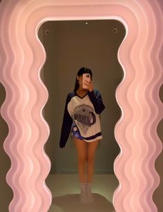 a woman is taking a selfie in front of a pink wall with wavy lines