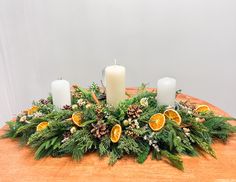 an arrangement of oranges, pine cones and greenery on a table with candles