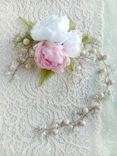 two white and pink flowers sitting on top of a lace covered table cloth with beads