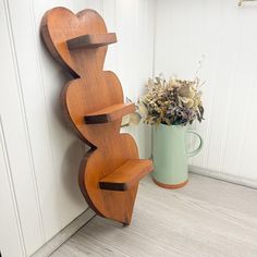 a wooden sculpture next to a vase with flowers in it on the floor near a wall