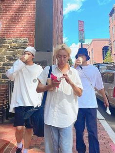 three young men walking down the street while looking at their cell phones in front of them