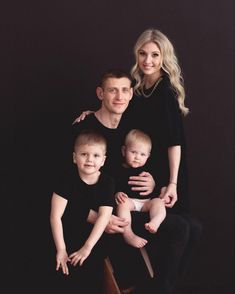 a family poses for a portrait with their two sons and one baby in front of a black background