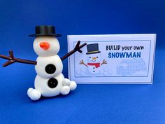 a snowman is sitting next to a card with the words build your own snowman on it